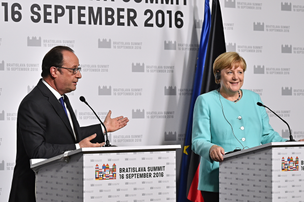 Bundeskanzlerin Angela Merkel und Frankreichs Präsident François Hollande vor zwei Podien mit Mikrofonen, beide lächelnd, mit einem 'Bratislava-Gipfel 2016'-Schild im Hintergrund.
