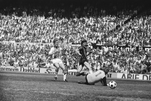 Schwarzes und weißes Bild von Männern, die auf einem Feld Fußball spielen, mit Zuschauern im Hintergrund und einer Tafel "Bundesliga 1978-79 Ajax 1-1 Hannover 96".