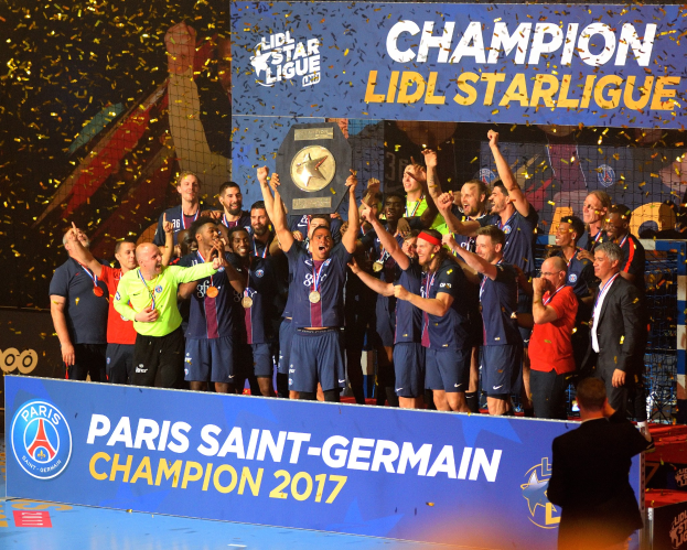 Eine Gruppe von Männern in Medaillen steht auf einem Basketballfeld und hält einen Pokal hoch, mit einer Tafel mit Text und Logos und einem Hintergrundbild, das den Sieg der Paris Saint-Germain Mannschaft in der Lidl Star League feiert.