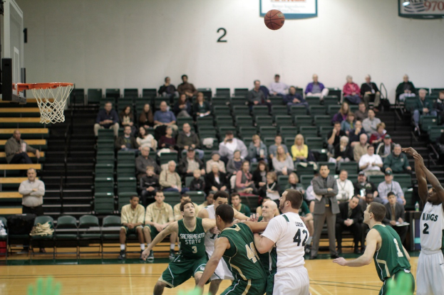 Ein Basketballfeld mit spielenden Spielern und Zuschauern im Hintergrund.