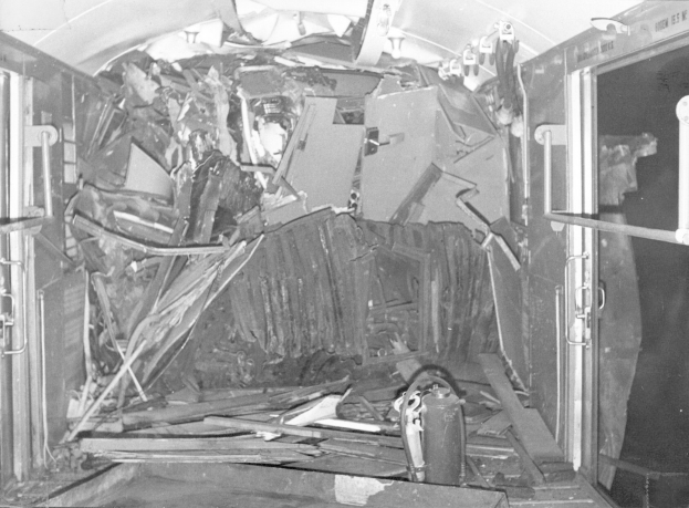 Schwarzes und weißes Foto eines zerstörten Zuginnenraums mit verstreuten Metallstangen, Lampen und Trümmern.