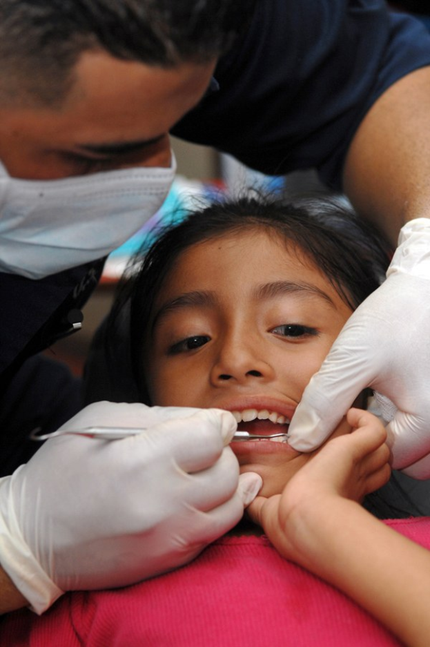 Ein junges Mädchen erhält eine zahnärztliche Untersuchung von einem maskierten Zahnarzt, der ein Instrument hält, mit einem unscharfen Hintergrund.