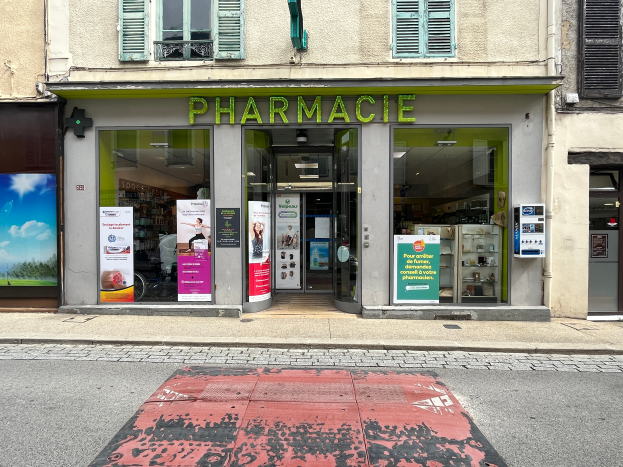 Eine Apotheke an einer Straßenecke mit Glaswänden und -türen, Plakaten an den Wänden und einer Straße davor.