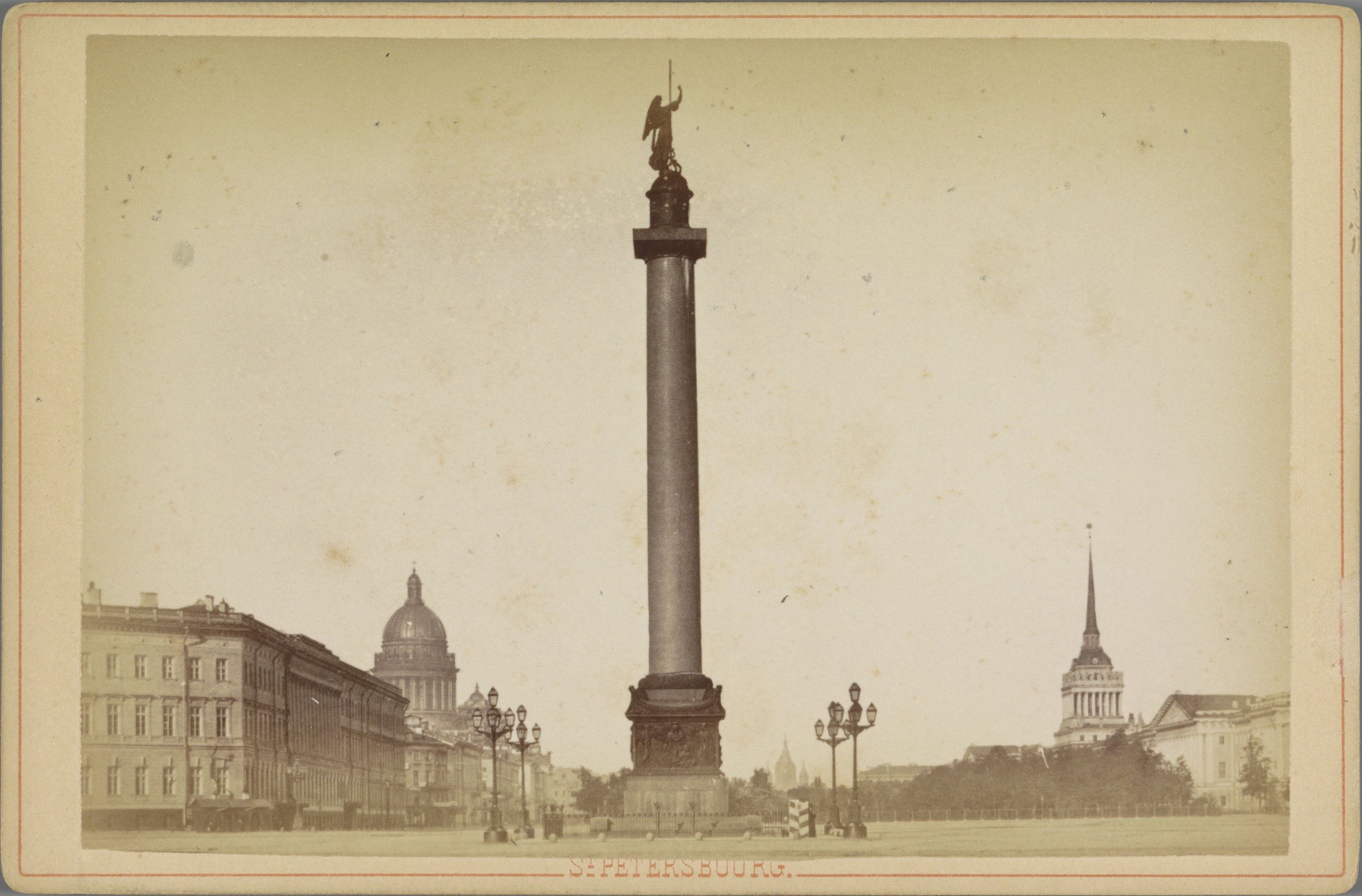 Altes Schwarz-Weiß-Foto eines Denkmals in einem städtischen Platz, eingerahmt von Gebäuden, Straßenmöbeln, Bäumen und einem klaren Himmel, mit Text entlang der unteren Kante.