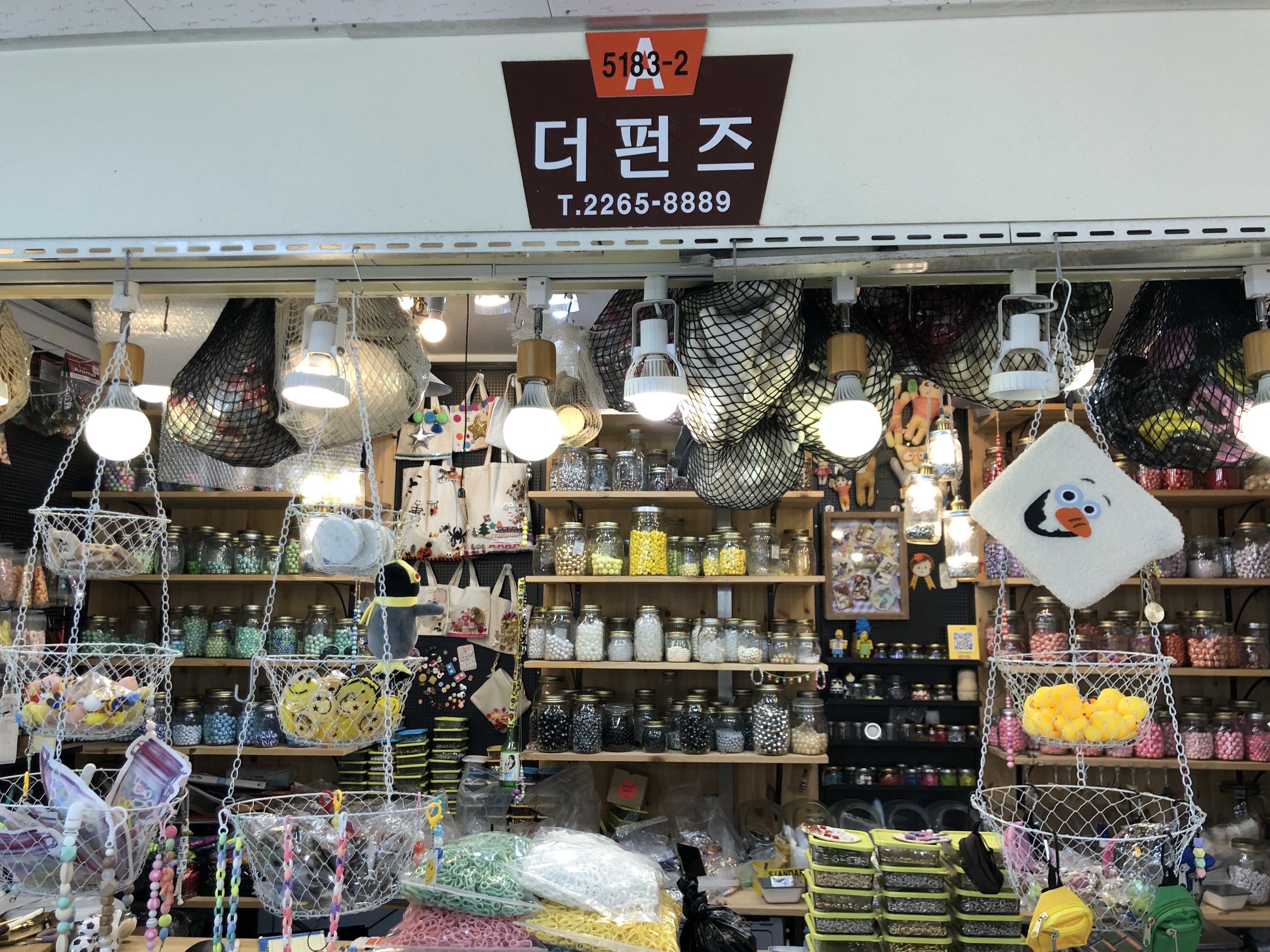 Ein unordentlicher Laden in Seoul mit verschiedenen Gegenst%C3%A4nden wie K%C3%B6rbchen, Lichtern, Flaschen und Spielzeugen auf Regalen, mit einer Tafel oben, die anzeigt, dass es einer der besten koreanischen L%C3%A4den ist.