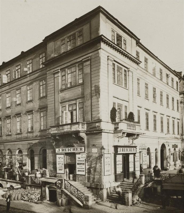Altes Backsteingebäude mit der Aufschrift 'J Reicher Hotel' in Berlin, mit Fenstern, Treppen mit Geländern, Informationsschildern, Topfpflanzen und einigen Menschen, mit Himmel im Hintergrund.