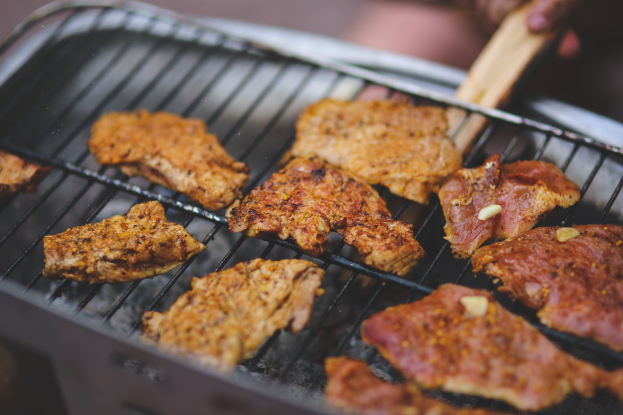 Person grilling meat on a barbecue grill using tongs, with a slightly blurred background.