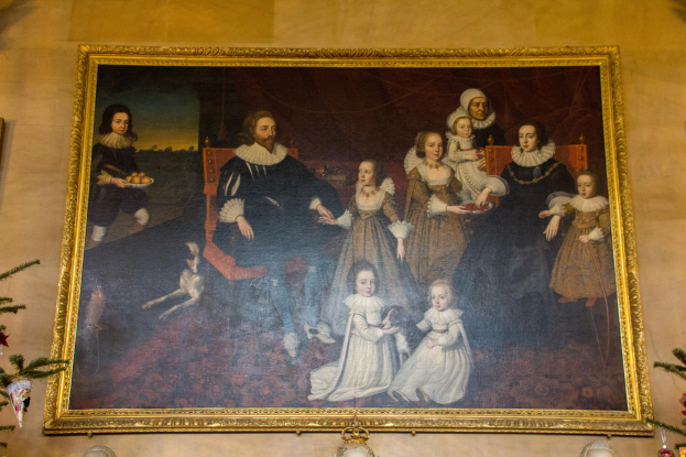 Ein gerahmtes Bild einer Familie mit einem Weihnachtsbaum im Hintergrund, flankiert von zwei Fotorahmen, mit festlichen Dekorationsgegenständen unten.