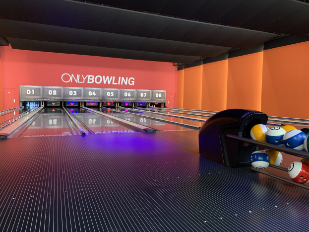 Eine Bowlinganlage mit Bowlingkugeln rechts, Kegeln in der Mitte und einer textbedeckten Wand im Hintergrund, mit der Decke darüber.