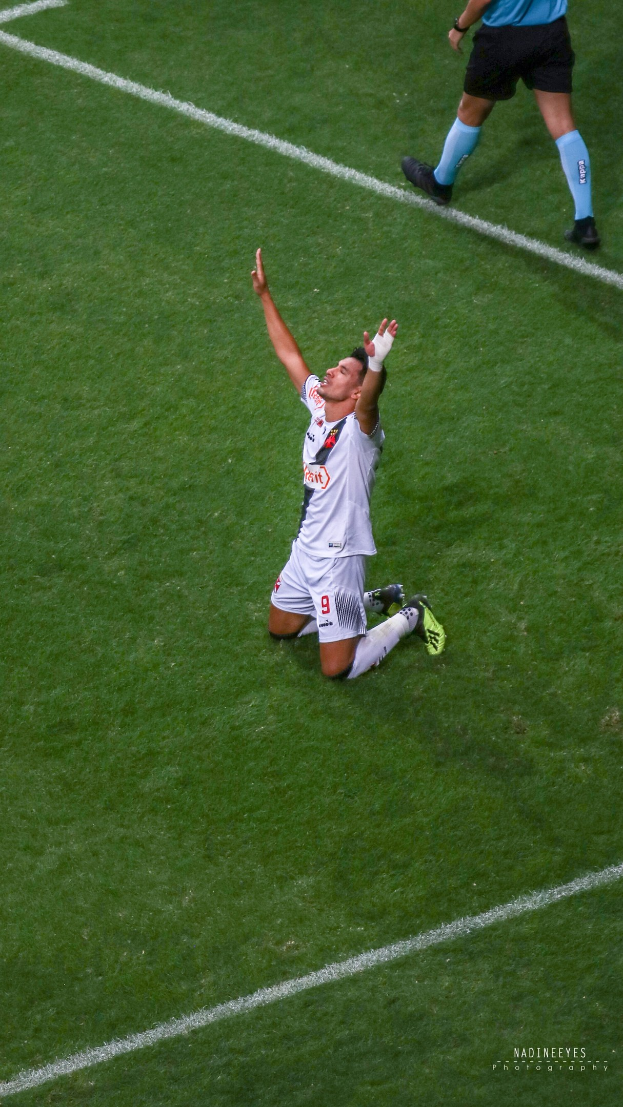 Fußballspieler in Uniform kniet auf dem Boden und feiert mit ausgestreckten Armen.