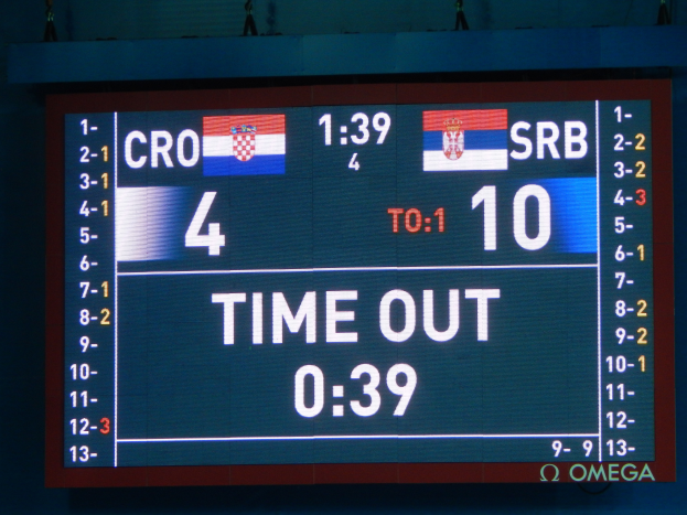 Ein großes elektronisches Scoreboard mit der Aufschrift "Kroatien vs. Serbien" mit Zahlen, Text und Flaggen, mit ein paar Zuschauern oben im Bild.