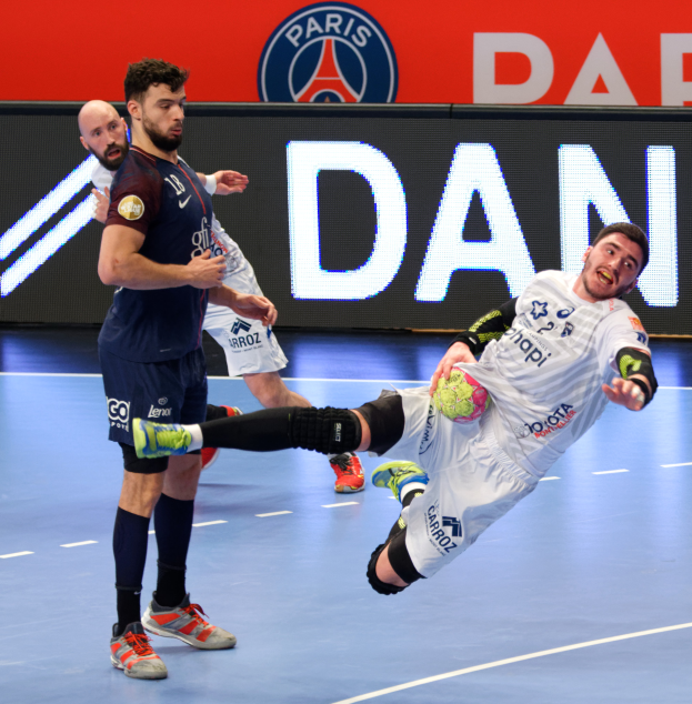 Eine Gruppe von Männern, die Handball auf einem Platz spielen, wobei einer den Ball hält, und ein Paris Saint-Germain-Futsal-Team-Schild im Hintergrund.