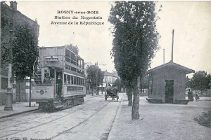 Ein altes Schwarz-Weiß-Foto einer Tram auf einer Straße in Rosny-sous-Bois, Frankreich, umgeben von Gebäuden, Bäumen, Pfählen und Menschen auf dem Gehweg, mit dem Himmel im Hintergrund und Text oben auf dem Bild.