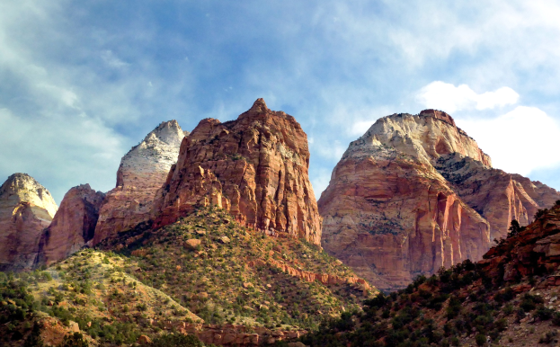 Eine malerische Aussicht auf den Zion-Nationalpark in Utah mit majestätischen Bergen, grünen Bäumen, felsigem Gelände und einem Himmel mit weißen Wolken.