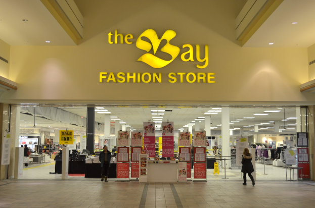 Außenansicht eines Bay Fashion Stores in einem Einkaufszentrum mit Kunden, Wandtafeln, tragenden Säulen, Deckenbeleuchtung und diversen Hintergrund-Elementen.