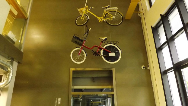 Zwei Fahrräder hängen von der Decke, ein Glasfenster auf der rechten Seite und ein Metallrohr auf der linken Seite in einem Gebäudeeingang.
