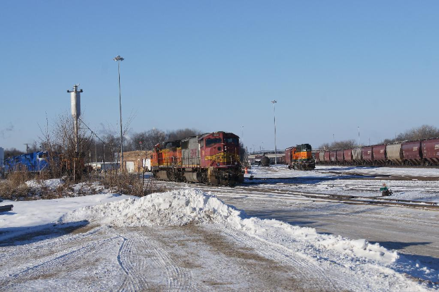 Eine Lokomotive vorne mit einem Waggon auf der rechten Seite, auf Schienen geparkt mit Schnee auf dem Boden, trockenen Bäumen und einem Strommast im Hintergrund.