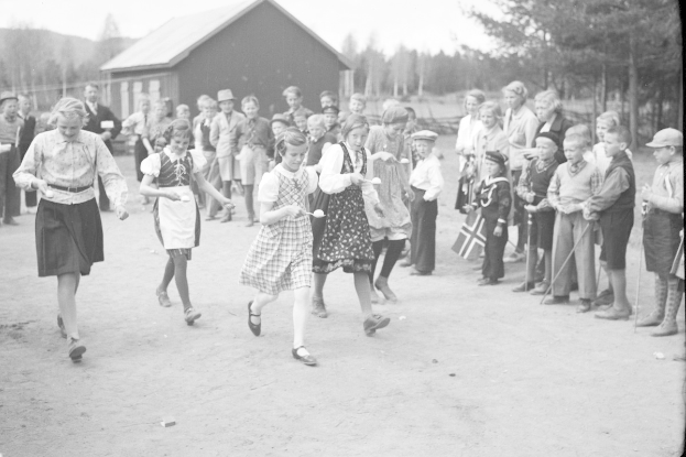 Schwarzes Bild von Kindern, die Fußball spielen, mit einer Menge, die Fahnen hält, Bäumen und einem Haus im Hintergrund.
