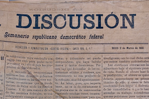 Eine vergilbte, leicht zerknitterte Zeitung mit der Aufschrift "Diskussion" in schwarzer Tinte, mit der √úberschrift "Semanario Rep√ļblicano Democr√°tico Federal".
