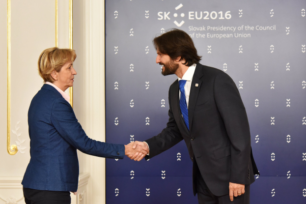 Bundeskanzlerin Angela Merkel und Bundeskanzler Joachim Gauck geben sich die Hand vor einer Wand mit einem "EU-Gipfel"-Schild und einer Tür im Hintergrund, beide l├Ącheln.