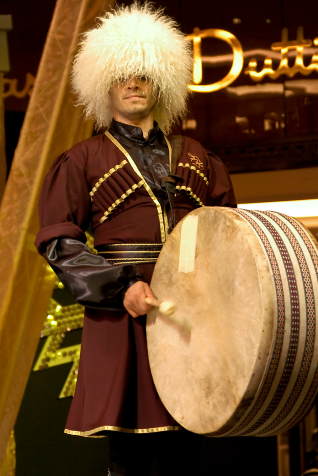 Ein Mann steht in der Mitte und schlägt auf ein Drumset ein, mit Lichtern und Text im Hintergrund.