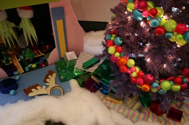 Innen, ein geschmückter Weihnachtsbaum mit Lichterkette und Schmuck steht rechts, mit Geschenkboxen und Schmuck in der Mitte, einer Hütte mit Schmuck oben links und Baumwolle und Wolle unten.