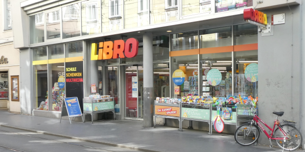 Ein Fahrrad, das vor einem Geschäft mit Glaswänden und -fenstern geparkt ist, das Schilder mit Text anzeigt, auf einer Straße.