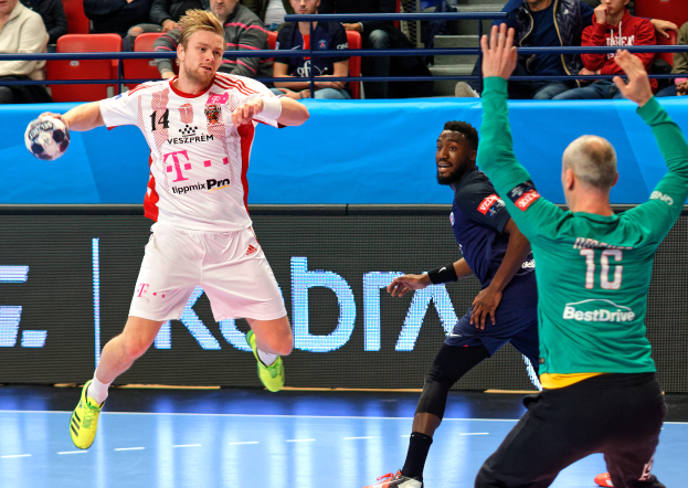 Eine Gruppe von Männern spielt Hallenfußball auf einem Platz mit einem Ball in der Mitte, während Zuschauer von Stühlen und Geländern in einer Halle zuschauen, mit einem Schild im Hintergrund mit der Aufschrift "Futsal-Weltmeisterschaft 2019 - Bayern München vs. Paris Saint-Germain."