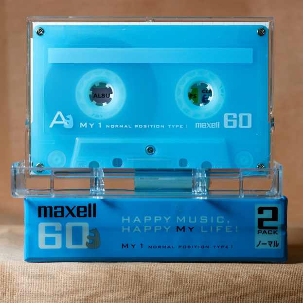 Blaue Kassette mit "Maxell Happy Music, Happy My Life" darauf, auf einer braunen Oberfläche platziert.