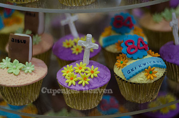 Ein Buch und ein heiliges Kreuzsymbol werden auf einem Cupcake plaziert, mit anderen Cupcakes im Hintergrund.