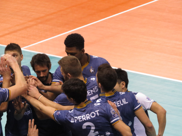 Eine Gruppe von Männern in blauen "Ligue 1"-T-Shirts feiert auf einem Volleyballfeld, einige mit erhobenen Händen.