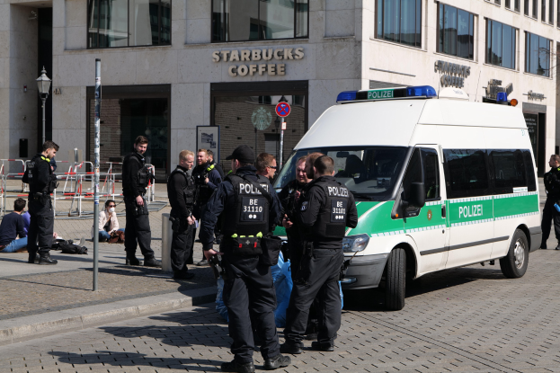 Polizeibeamte vor einem Starbucks-Café mit einem Van auf der rechten Seite und Menschen auf der linken Seite, mit einem Gebäude, einem Schild, einem Laternenpfahl und einem Zaun im Hintergrund.