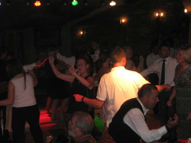Eine lebendige Partyszene mit tanzenden Menschen auf dem Boden unter verschiedenen bunten Lichtern in einem dunklen Raum.