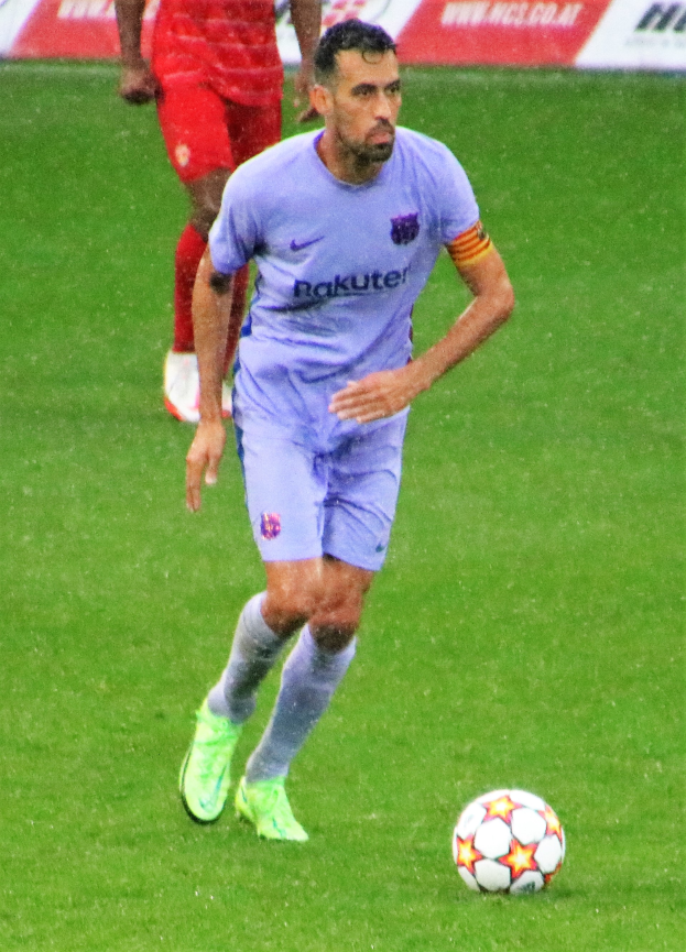 Ein Fussballspieler in Sportkleidung und Stutzen ist im Einsatz auf dem Feld, mit einem Textschild im Hintergrund.
