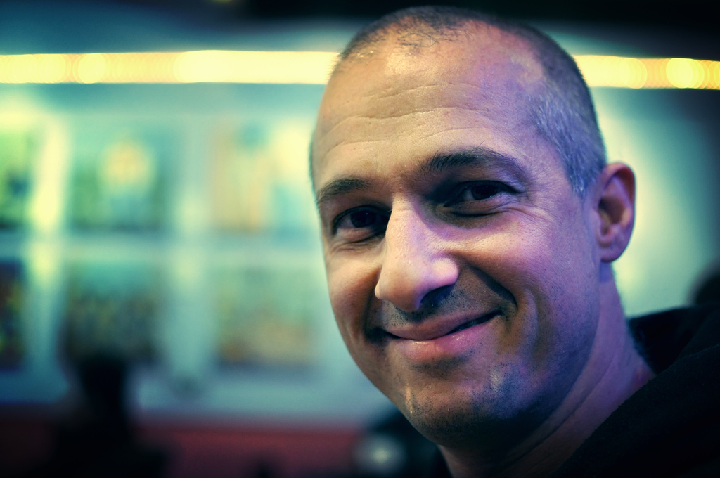 Ein Mann in einem schwarzen Kleid lacht mit einem unscharfen, hell beleuchteten Hintergrund.