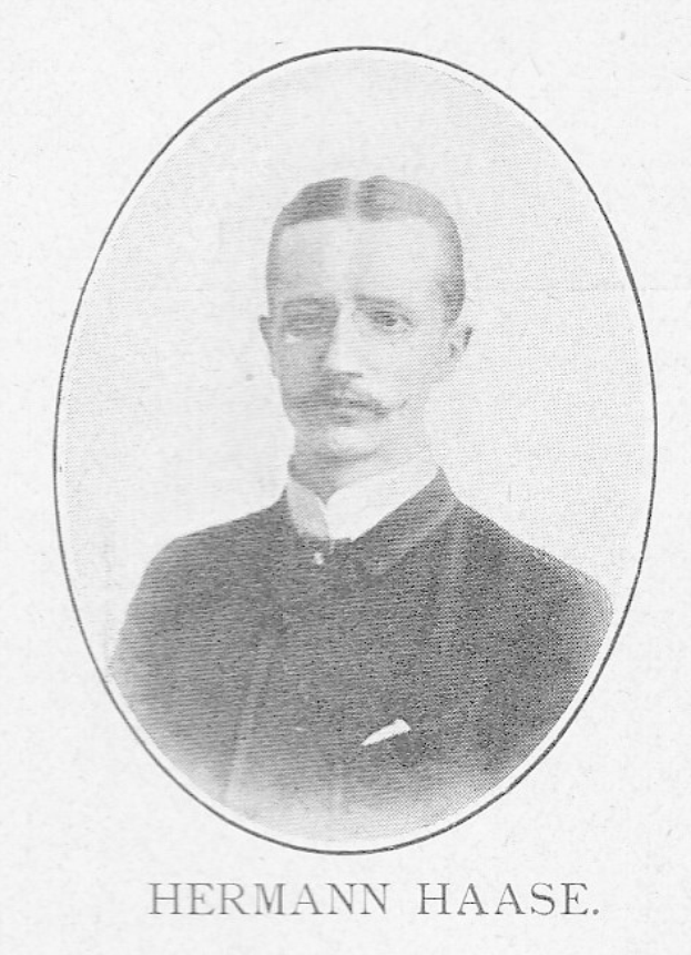 Ein Schwarz-Weiß-Foto eines Mannes mit Schnurrbart, identifiziert als Hermann Haase, ein deutscher Komponist und Pianist, der einen Anzug trägt und einen ernsten Gesichtsausdruck hat, mit deutschem Text unten.