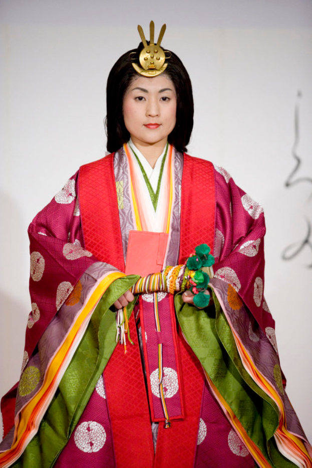 Eine Frau in einem traditionellen japanischen Kimono, mit einem leuchtend roten und grünen Kleid mit aufwändigen Mustern, steht selbstbewusst auf einem Laufsteg, ihr Haar ist zu einem ordentlichen Knoten gebunden.