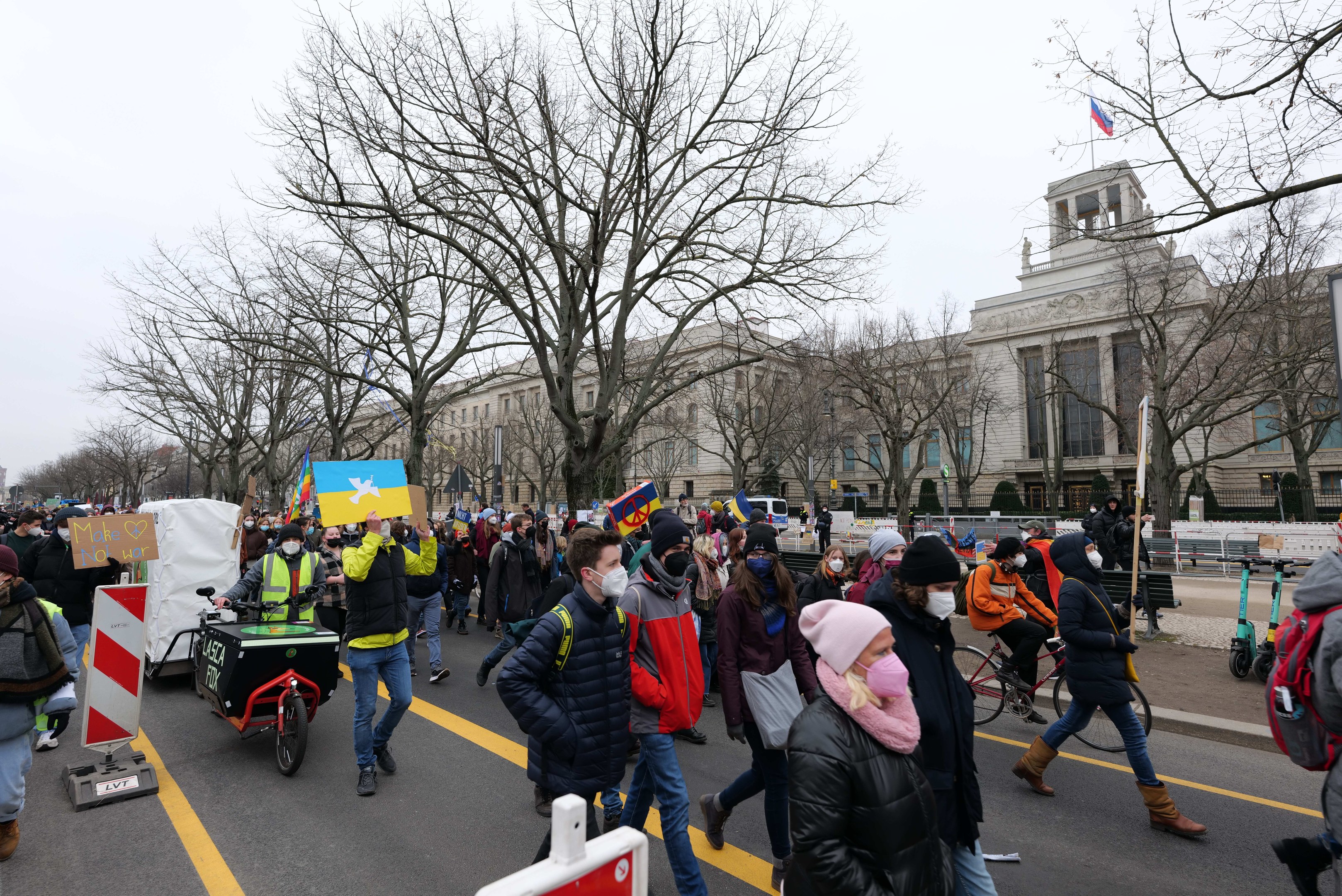 Eine große Gruppe von Menschen nimmt an einer Protestmarsch in Washington, D.C. am 21. Januar 2020 teil, geht eine Straße entlang und hält Plakate und Schilder in die Höhe, während andere Fahrräder fahren, mit Schilderständen, Bäumen und einem klaren blauen Himmel im Hintergrund.