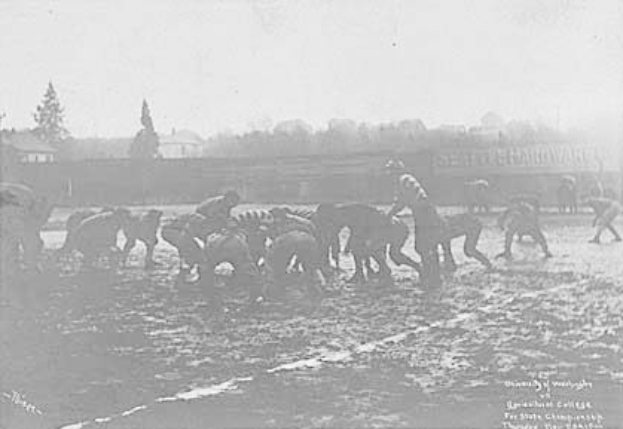 Ein Schwarz-Weiß-Foto von Menschen, die Fußball auf einem Feld spielen, mit Pferden im Vordergrund und Bäumen, Gebäuden und Himmel im Hintergrund, datiert 1918-1918 Fußball an der Staatsuniversität.