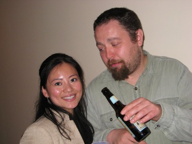 Mann mit Flasche starrt lächelnde Frau vor Wandhintergrund an.