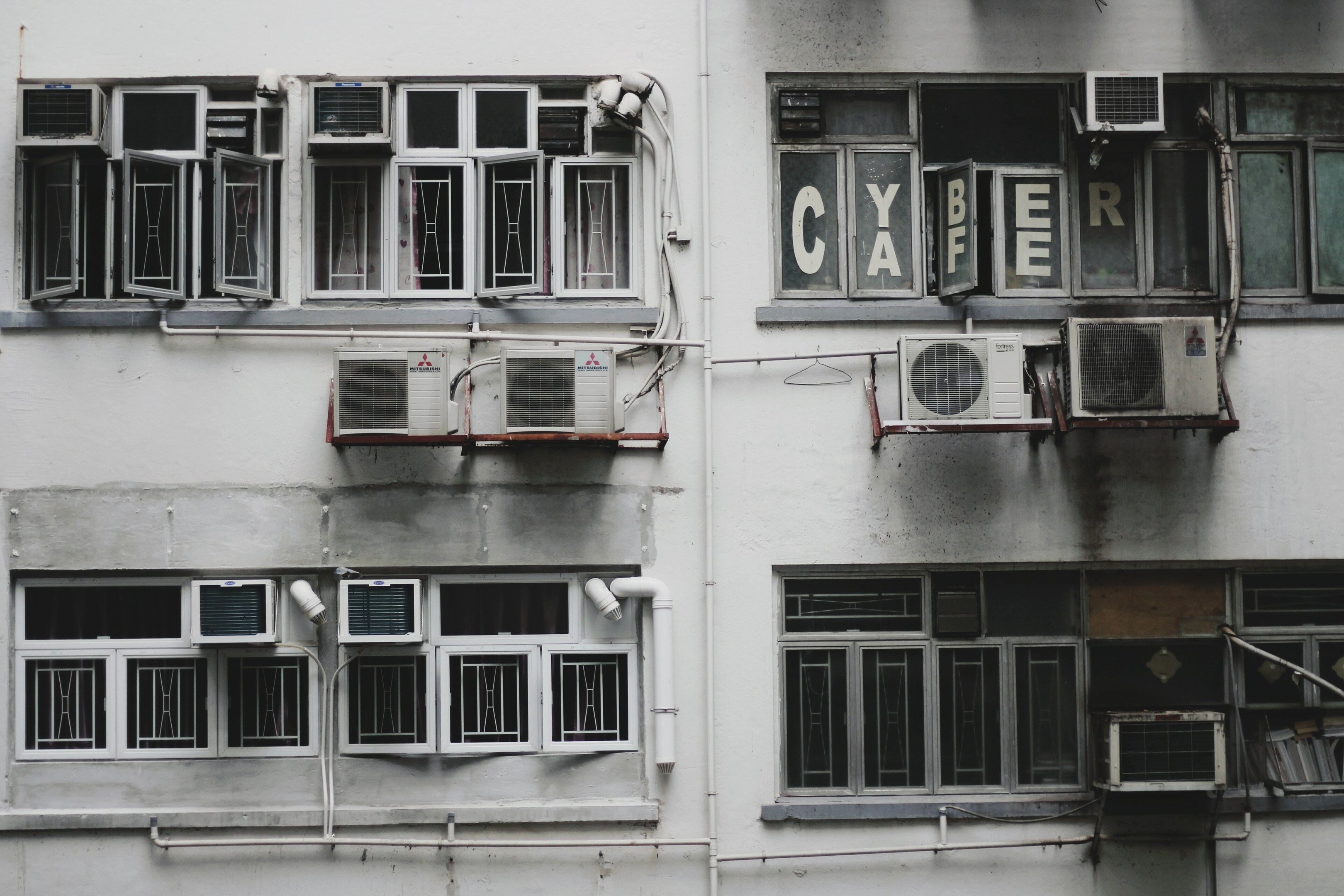 Altes Gebäude mit zahlreichen Fenstern, wandmontierten Klimaanlagen und äußeren Rohren.