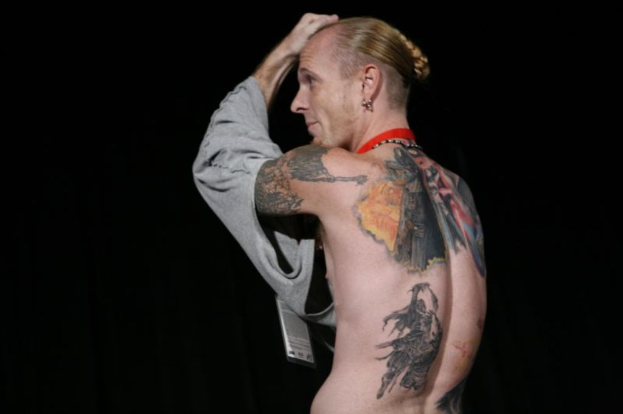 Eine Frau mit sichtbaren Tattoos auf ihrem Körper, mit Text oben und unten im Bild und einem unscharfen Hintergrund.