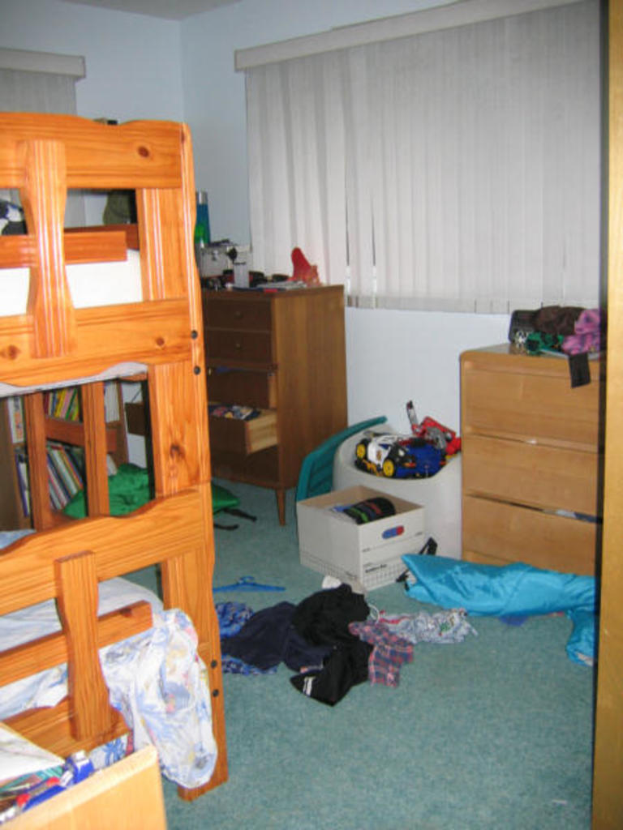 Ein Zimmer mit einem Etagenbett, Schreibtisch, Tisch und verstreuten Kleidern und Gegenständen auf dem Boden.