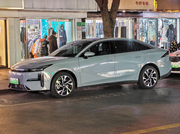 Ein Mitsubishi Lancer EV Elektroauto auf der Straße bei Nacht geparkt, umgeben von Gebäuden, Geschäften, Schaufensterpuppen mit Kleidern, Schildern mit Text, Lichtern und anderen Gegenständen.