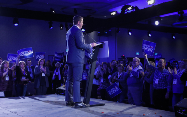Ein Mann spricht auf einem Podium mit einem Mikrofon vor einer Menge mit Schildern und Applaus während einer Wahlveranstaltung.