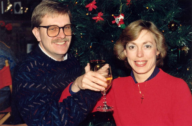 Ein Paar lächelt, waßrend es Gläser mit Wein hält, mit einem Weihnachtsbaum im Hintergrund.