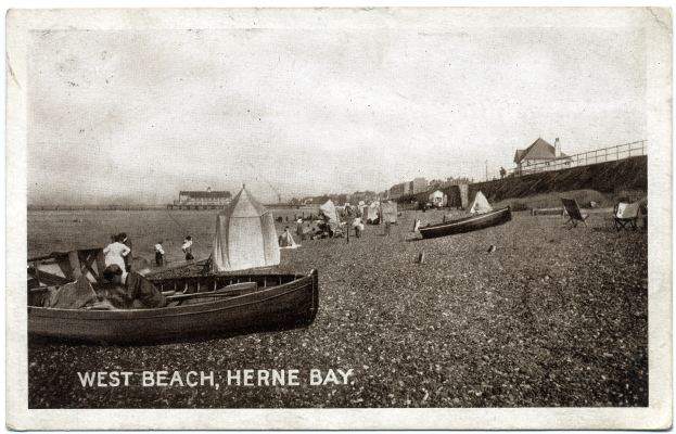 Schwarz-weiß-Foto von Menschen am Weststrand in Herne Bay mit Booten im Vordergrund, H├Ąusern und einem Zaun im Hintergrund und Text unten.