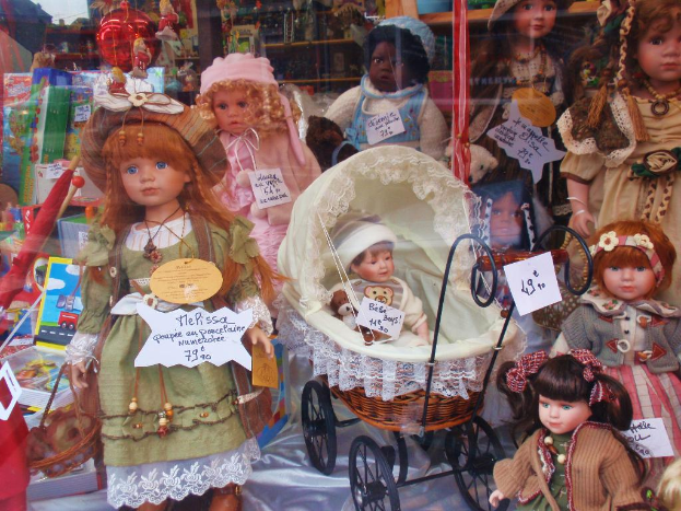 Eine Ausstellung mit mehreren Barbie-Puppen in bunten Kleidern, einem Rollstuhl, Kartons, einem Schirm, Ständern, Bannern und anderen Produkten.