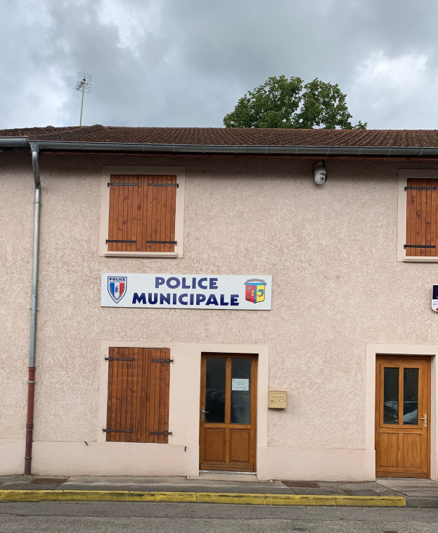 Polizeigebäude mit einem Schild, Fenstern, Türen, einer Namensschild, einem Rohr, einem Baum und einem wolkenverhangenen Himmel im Hintergrund.