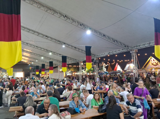 Eine gro%C3%9Fe Gruppe von Menschen an Tischen unter einem Zelt auf dem Oktoberfest in M%C3%BCnchen, Deutschland, mit festlichen Dekorationen im Hintergrund.